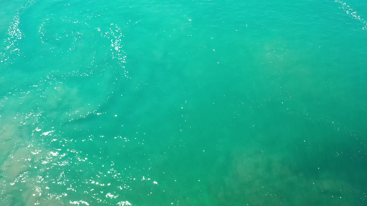 Overhead Los Cabos water frame with a pale submerged patch near the center left, scattered ripples, and no visible people.