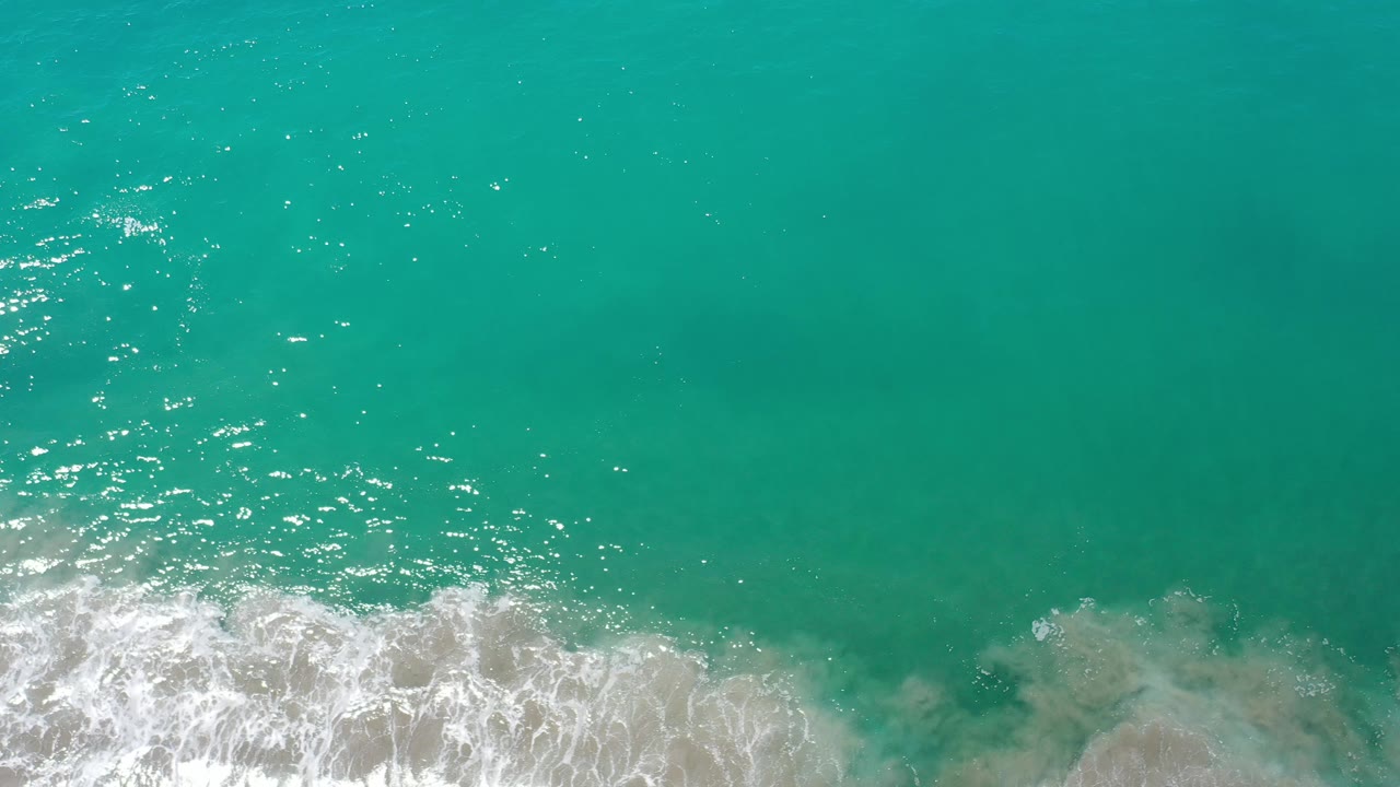 Clear turquoise water with surf foam and darker underwater patches.