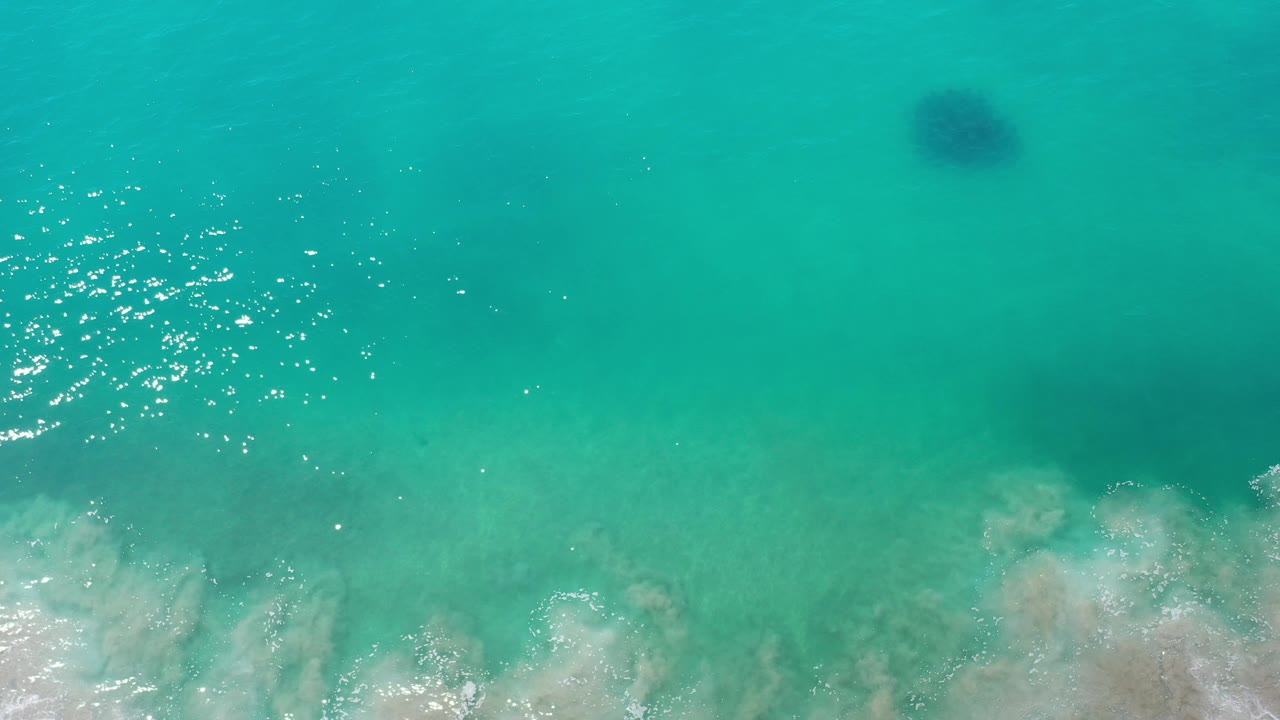 Clear green ocean with a dark circular underwater shape above foamy surf.