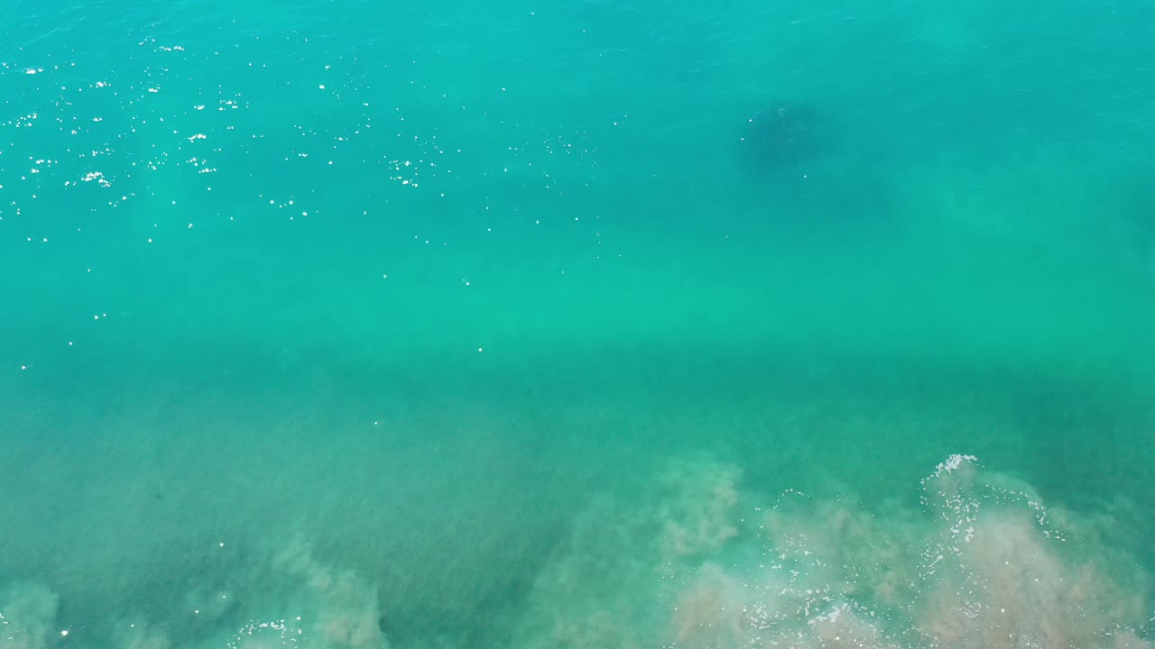 Aerial frame of green ocean water in Los Cabos, Mexico, with soft foam near the bottom and darker submerged shapes visible under the surface, no visible people.