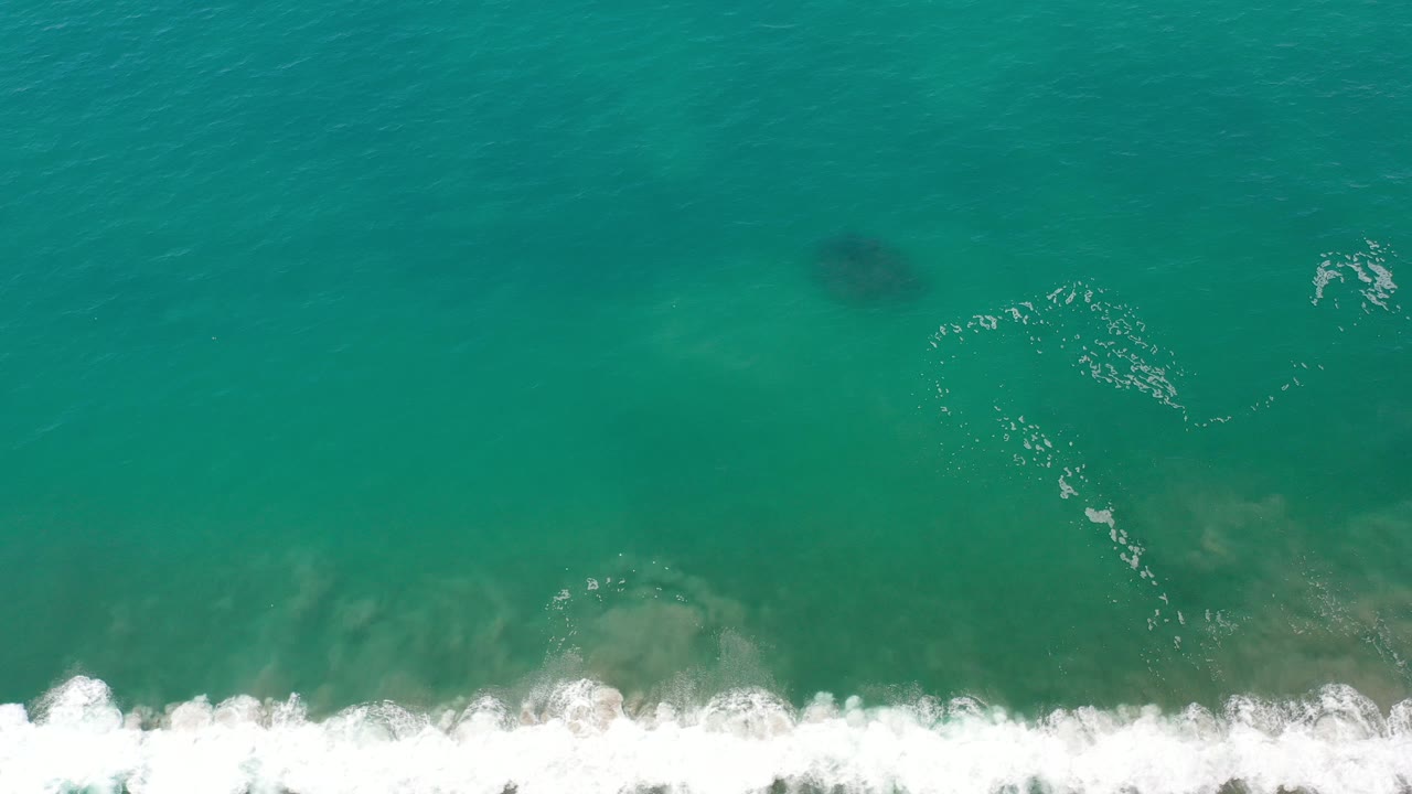 Overhead view of green ocean water in Los Cabos with white foamy surf entering along the lower edge and no visible people.