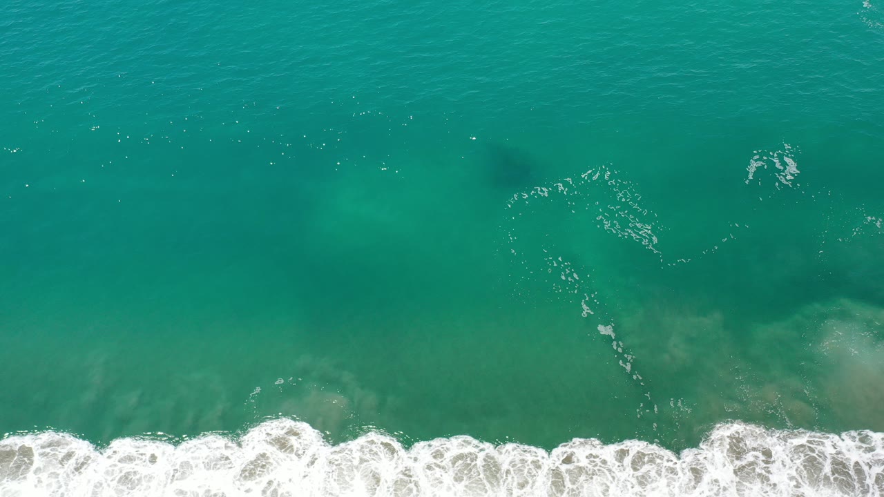 Overhead view of green ocean water in Los Cabos, Mexico, with white surf breaking along the bottom edge and no visible people.