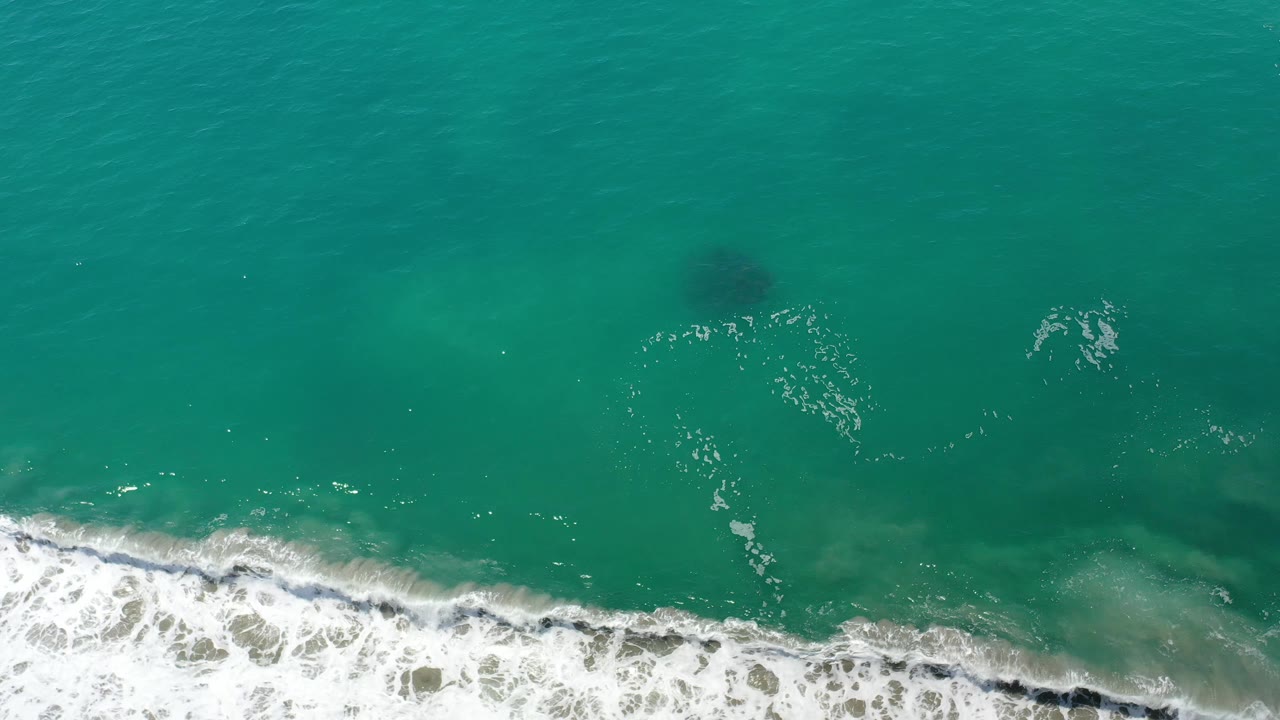 Turquoise sea with white foam and cloudy darker water near the shoreline.