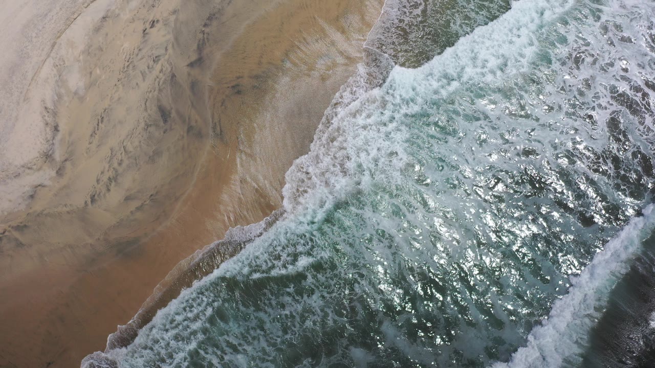 Overhead surf washing onto tan beach sand