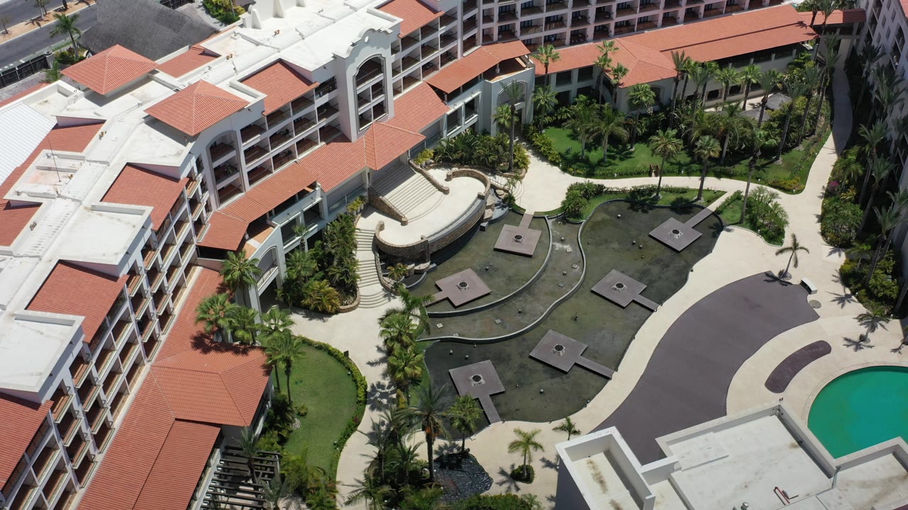 Aerial view of white buildings with red tile roofs around a landscaped courtyard.