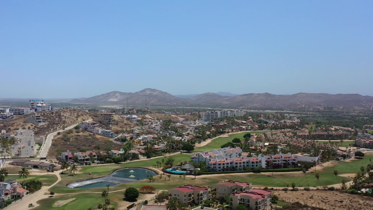 Aerial view of golf greens, homes, dry hills, and distant mountains.