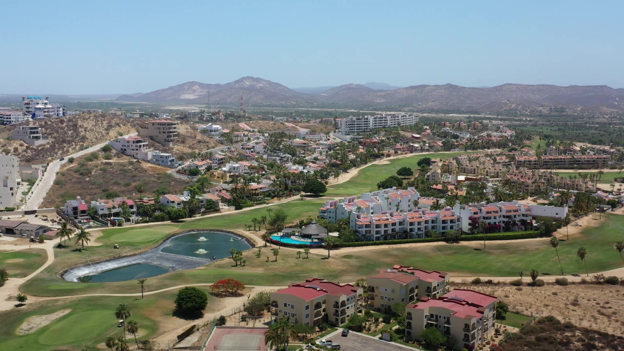 Los Cabos drone-style view centered on fairways and ponds, with resort suites across the midground, hillside construction, and no visible people.