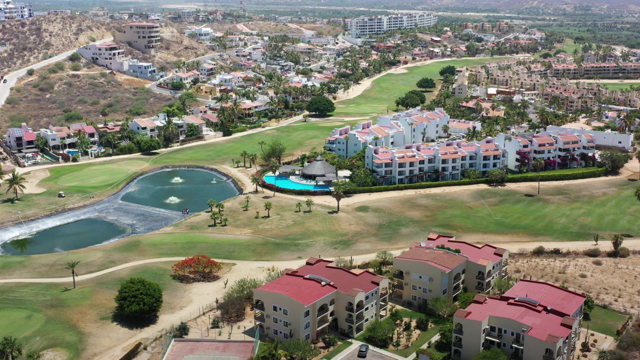 Aerial view of golf course ponds, rooftops, roads, and residential buildings.