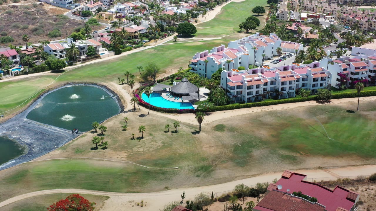 Aerial view of villas, pool, pond, and green landscaping.