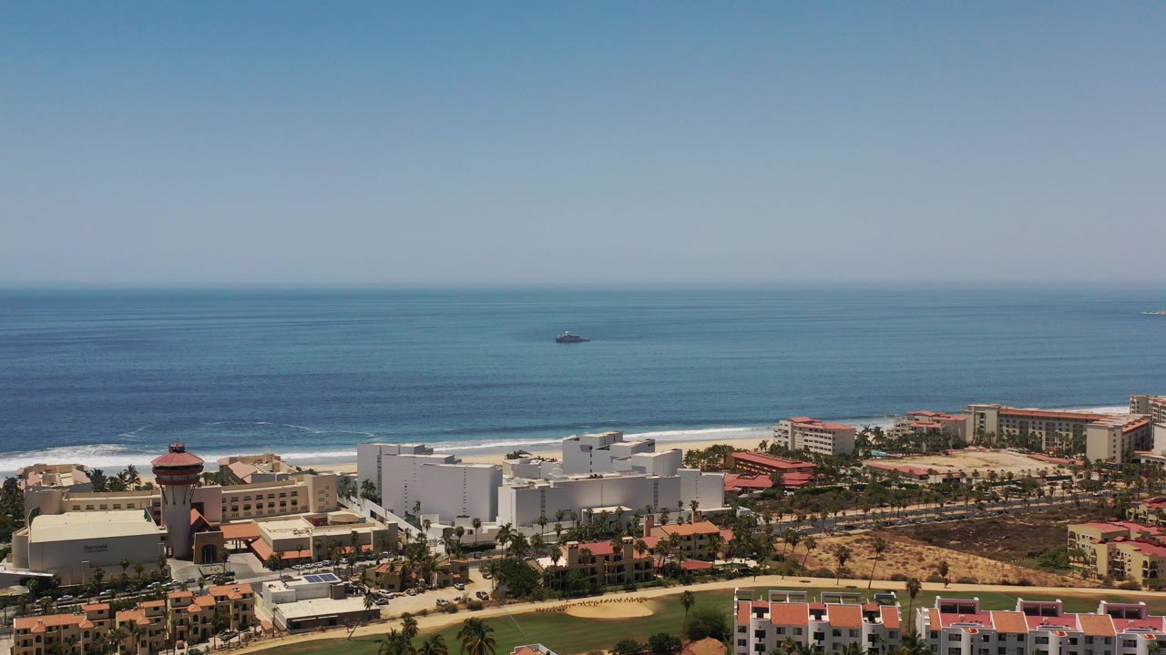 High coastal view with ocean, beachfront buildings, and red roofs.