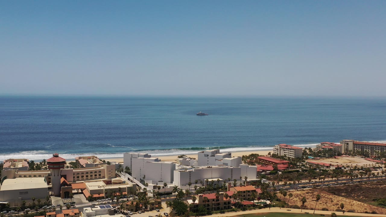 Beachfront resort-town buildings below calm blue water.