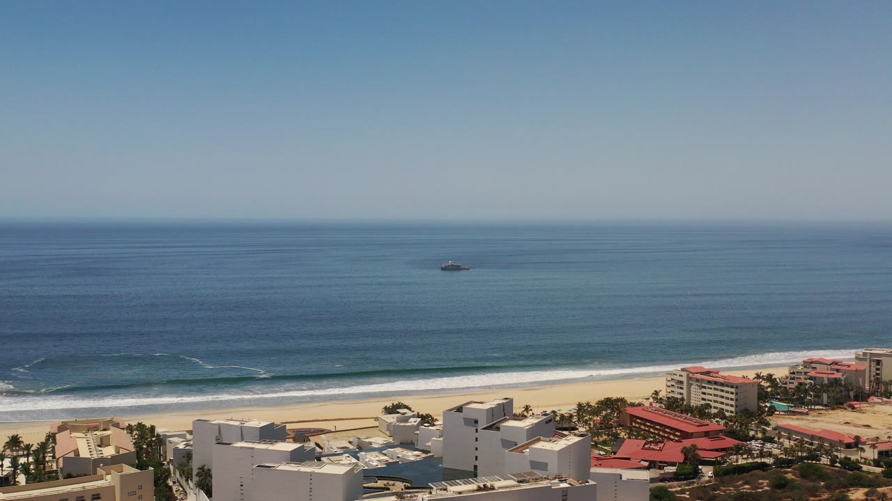 Wide coastal view of blue ocean, surf, beach, and resort buildings.