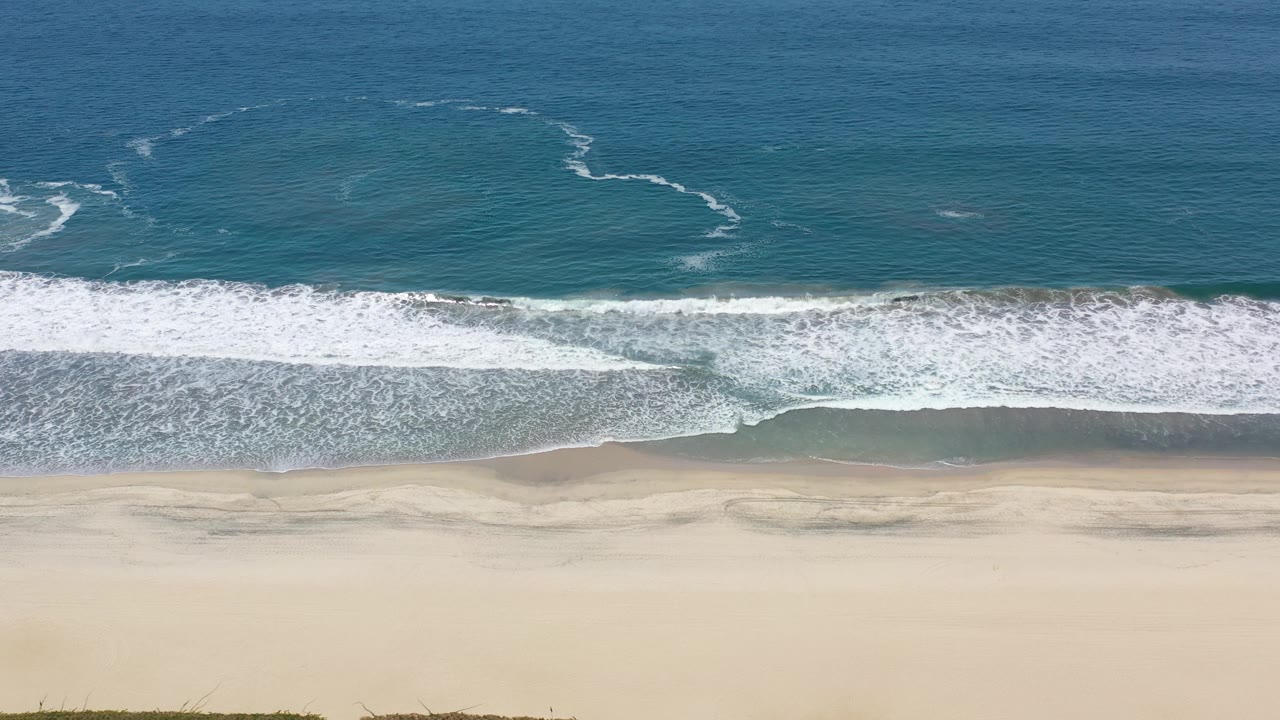 Aerial Los Cabos shoreline frame with the surf pushed farther onto the wet sand and no visible people on the beach.