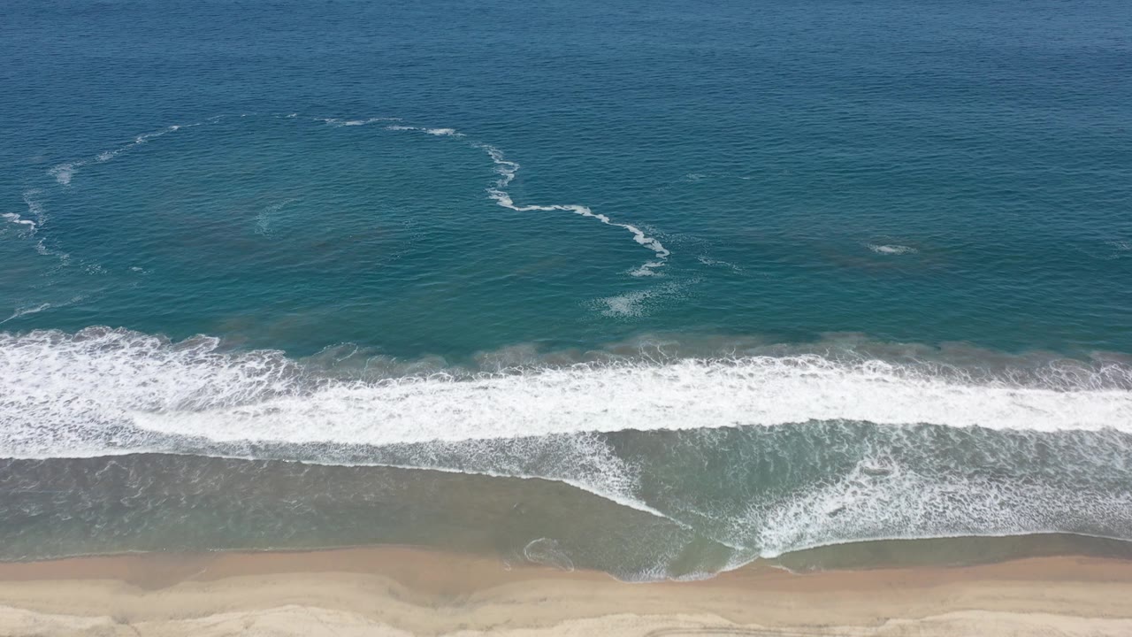 Aerial shoreline with curved foam patterns over green sea.