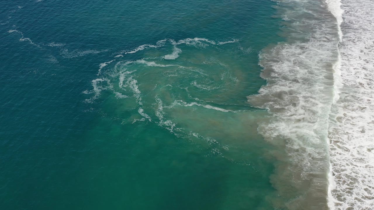 Aerial view of curling foam and turquoise surf near sand.