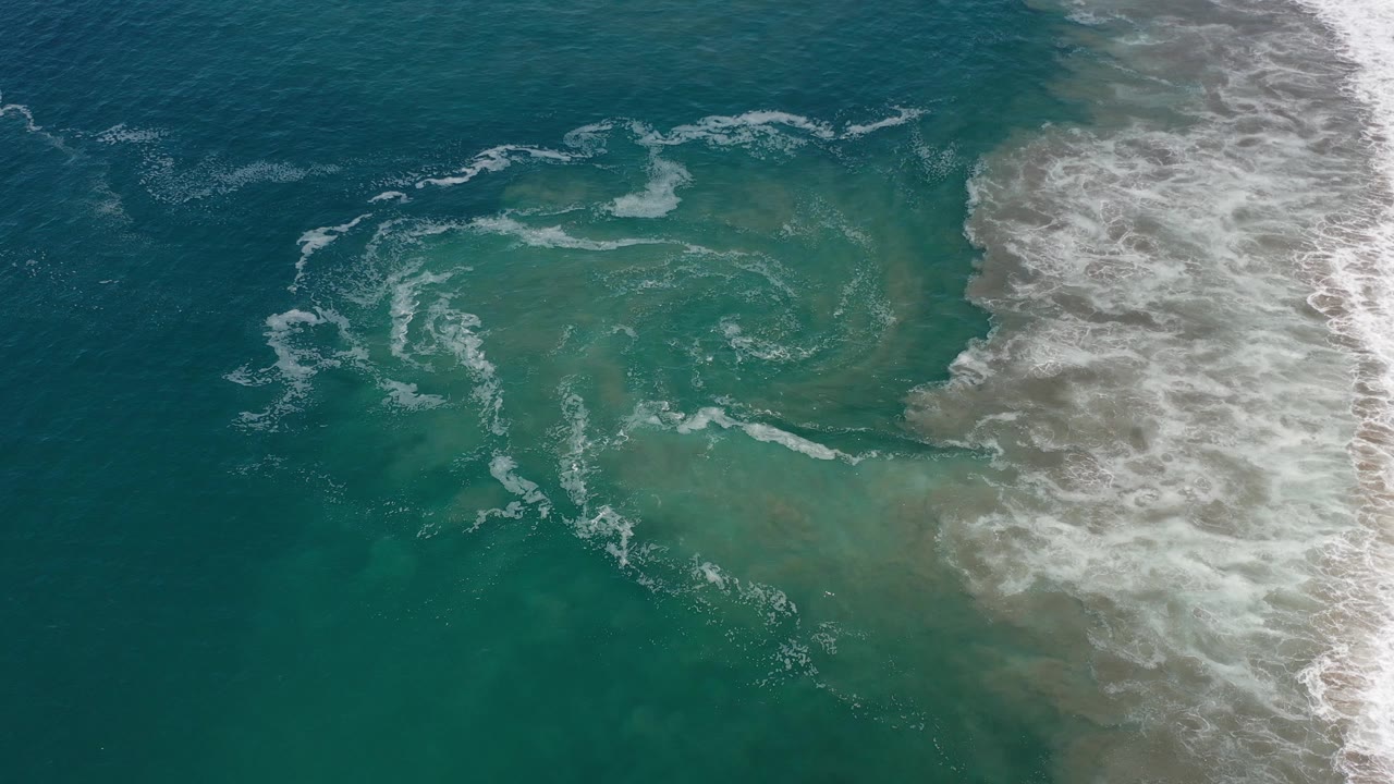 Top-down ocean surf with a pale circular swirl in green water.