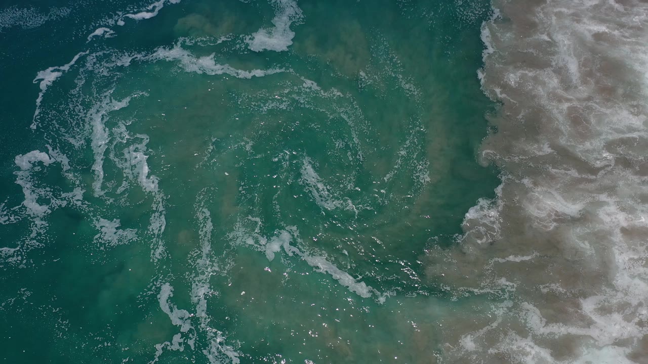 Top-down ocean surface with scattered foam and bright surf on the right.