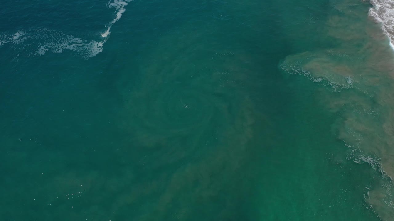 Top-down ocean view with rocky shore and light surf foam.