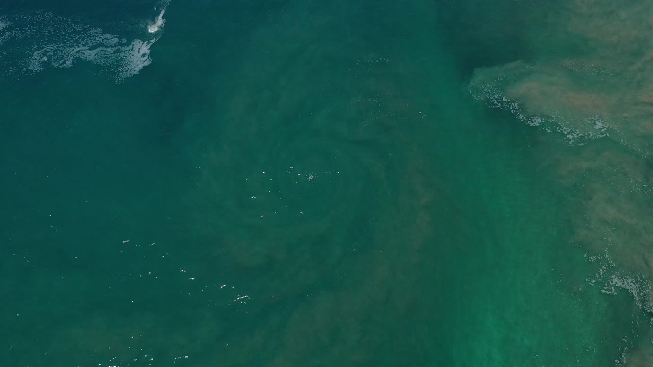 Overhead view of green water in Los Cabos, Mexico, with pale underwater patches near the upper right and no visible people.