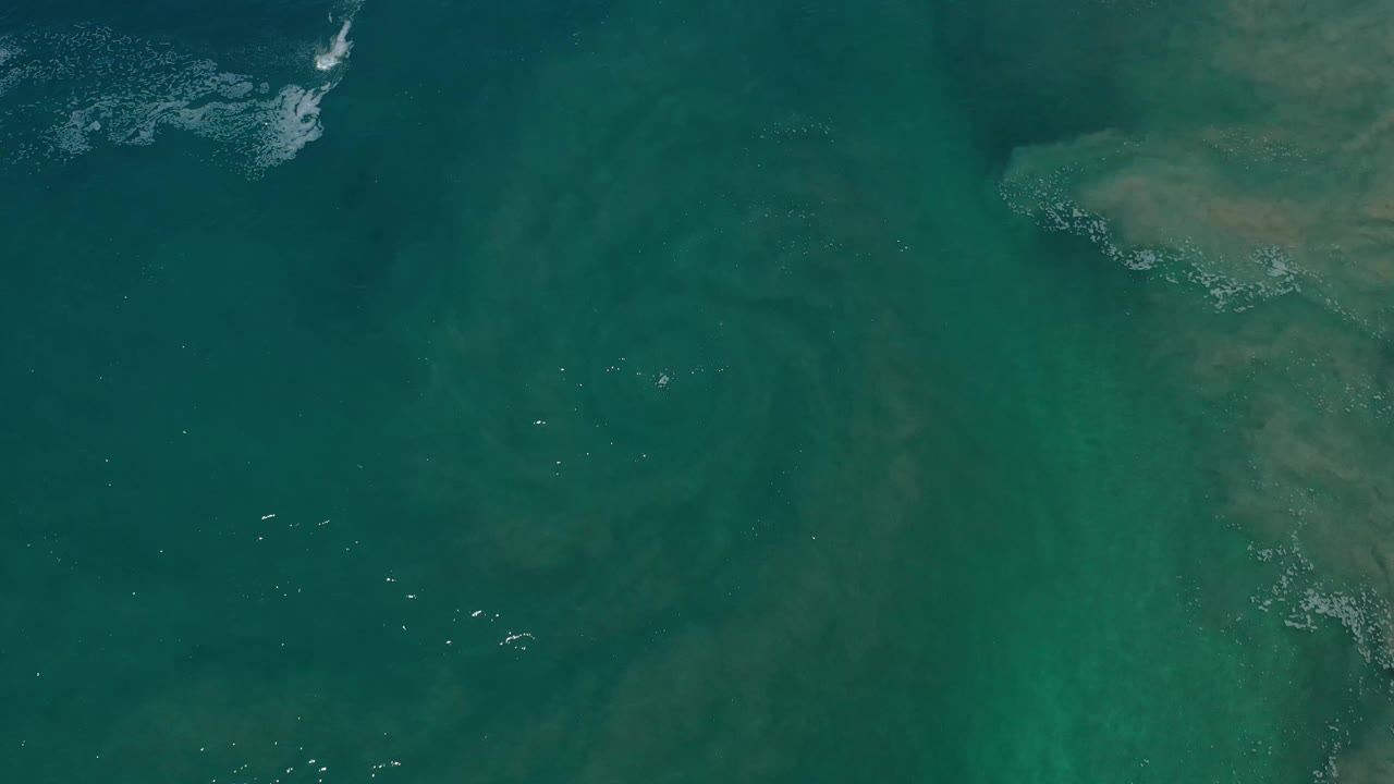 Aerial Los Cabos water view with faint tan-green submerged forms, darker teal areas, and no visible people.