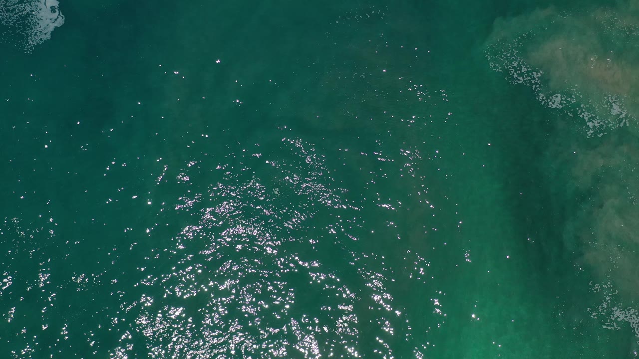 Overhead ocean surface with clustered sparkles and faint foam traces.