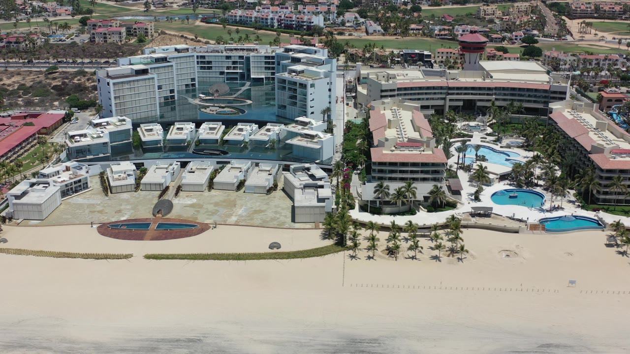 Modern coastal buildings beside a sandy beach and resort pool area.
