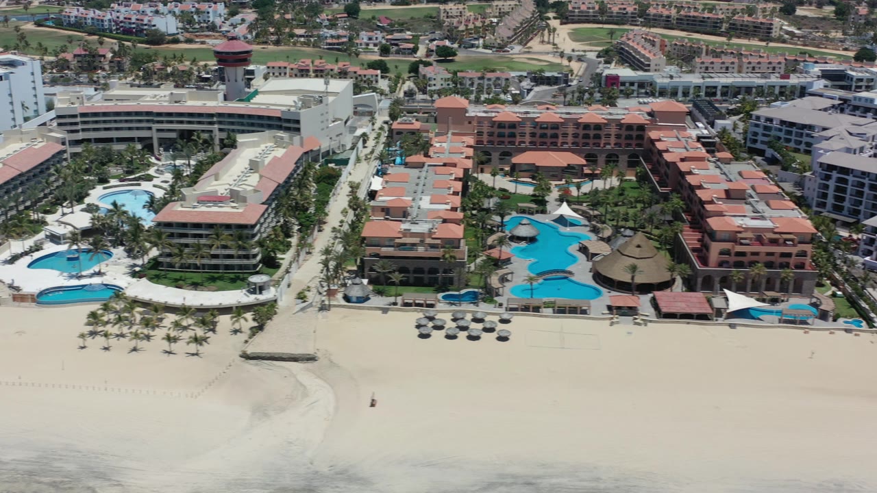 Beachfront hotel complex with pools and inland development behind it.
