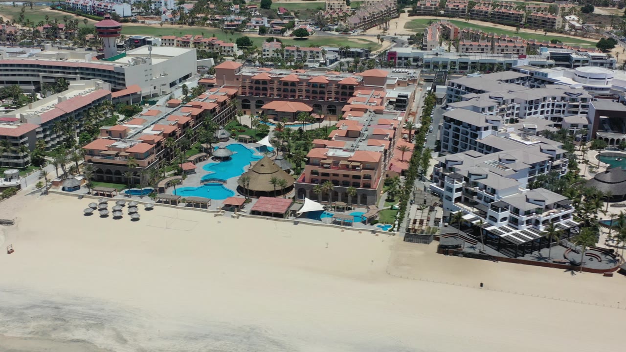 Aerial view of beachfront resorts with pools and wide sand.
