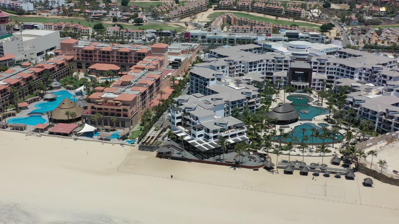 Aerial view of beachfront resort buildings, pools, and sand beach.