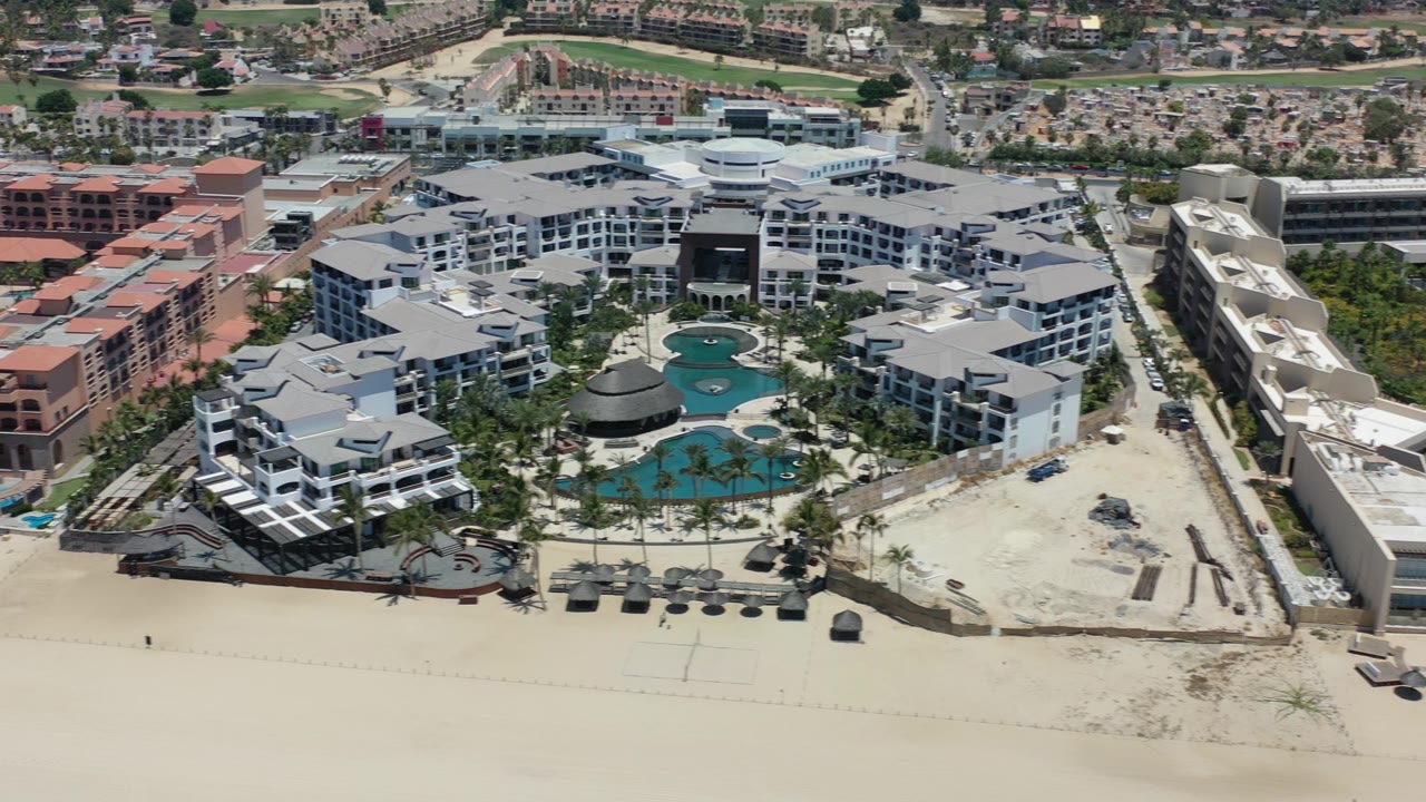 Aerial view of a beachfront resort with pools and pale sand.