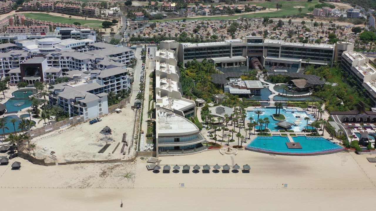 Aerial view of beachfront hotel buildings, pools, palms, and sand.