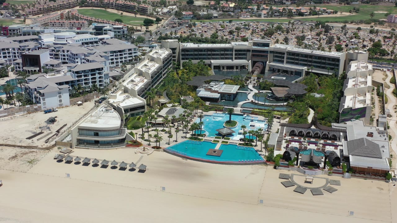 Aerial view of a beachfront resort with pools, cabanas, and pale sand.