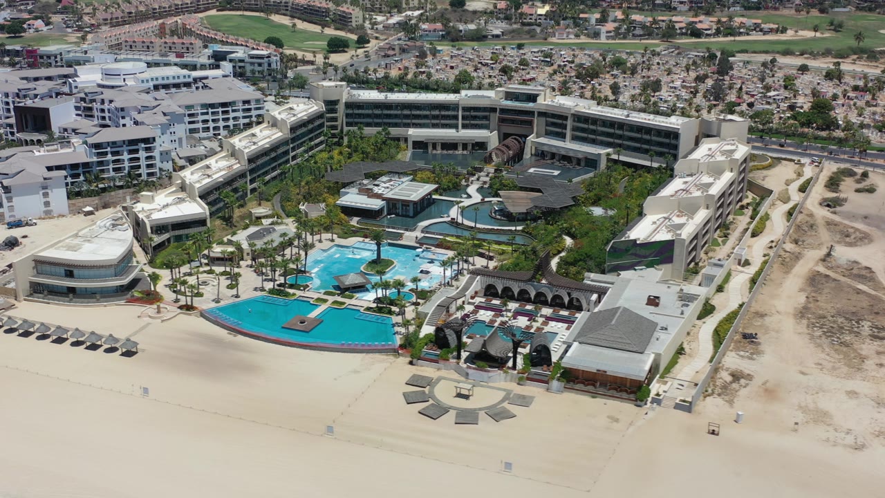 Beachfront resort complex with pools, sand, and city blocks behind.