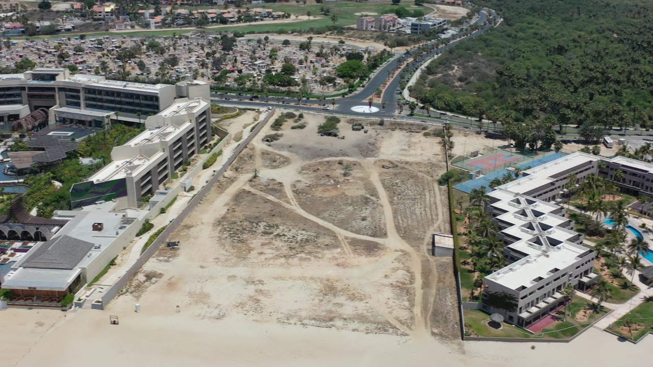 Beachfront lot with resort-style buildings, pool area, road, and dense greenery.