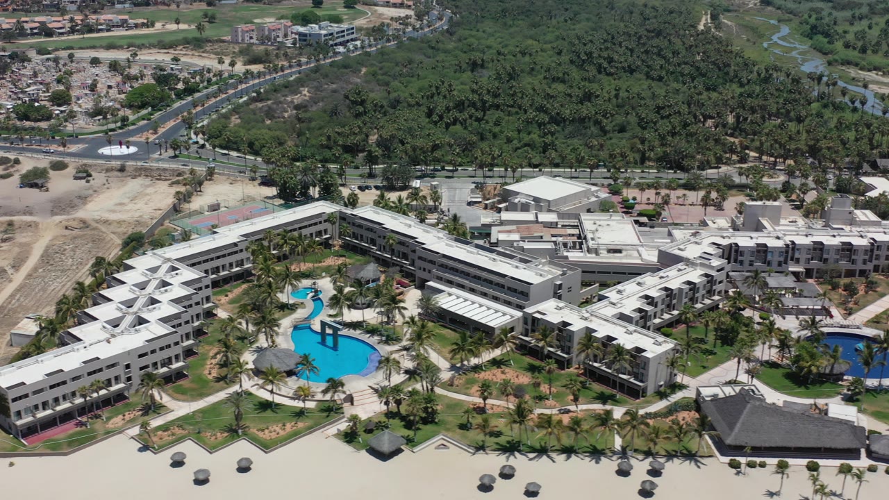 Aerial view of a beachfront resort complex with pools and palm landscaping.