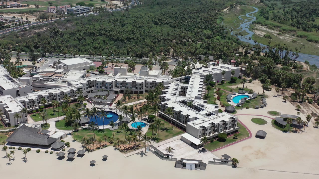 Aerial view of resort buildings, pools, sand, and dense trees.