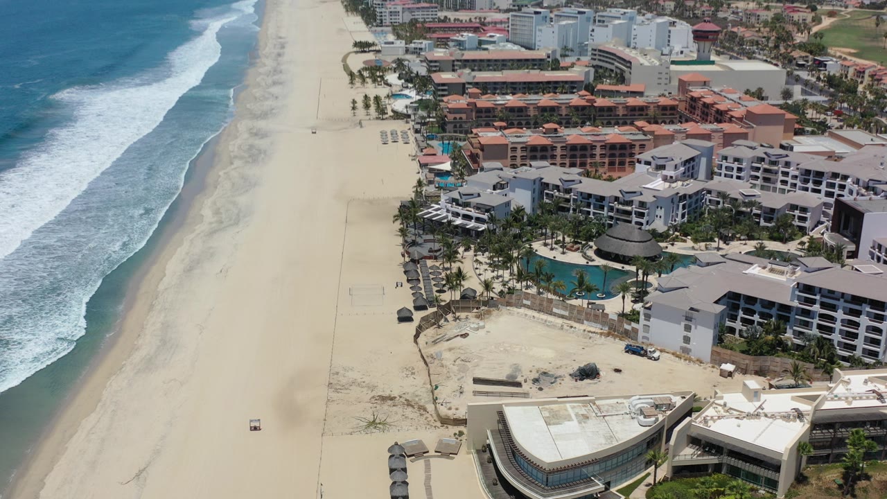 Aerial view of surf, sandy beach, and beachfront rooftops.