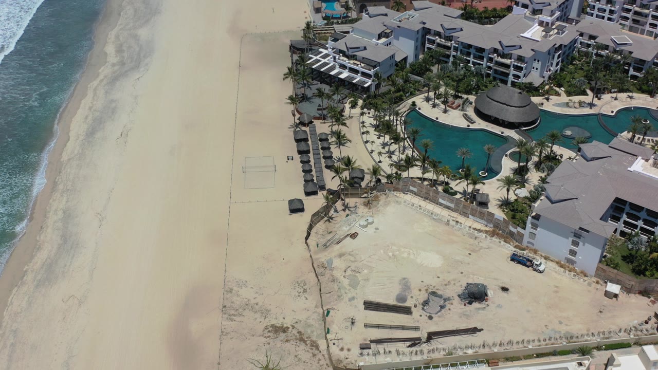 Aerial view of beach, surf, resort pools, and gray-roofed buildings.