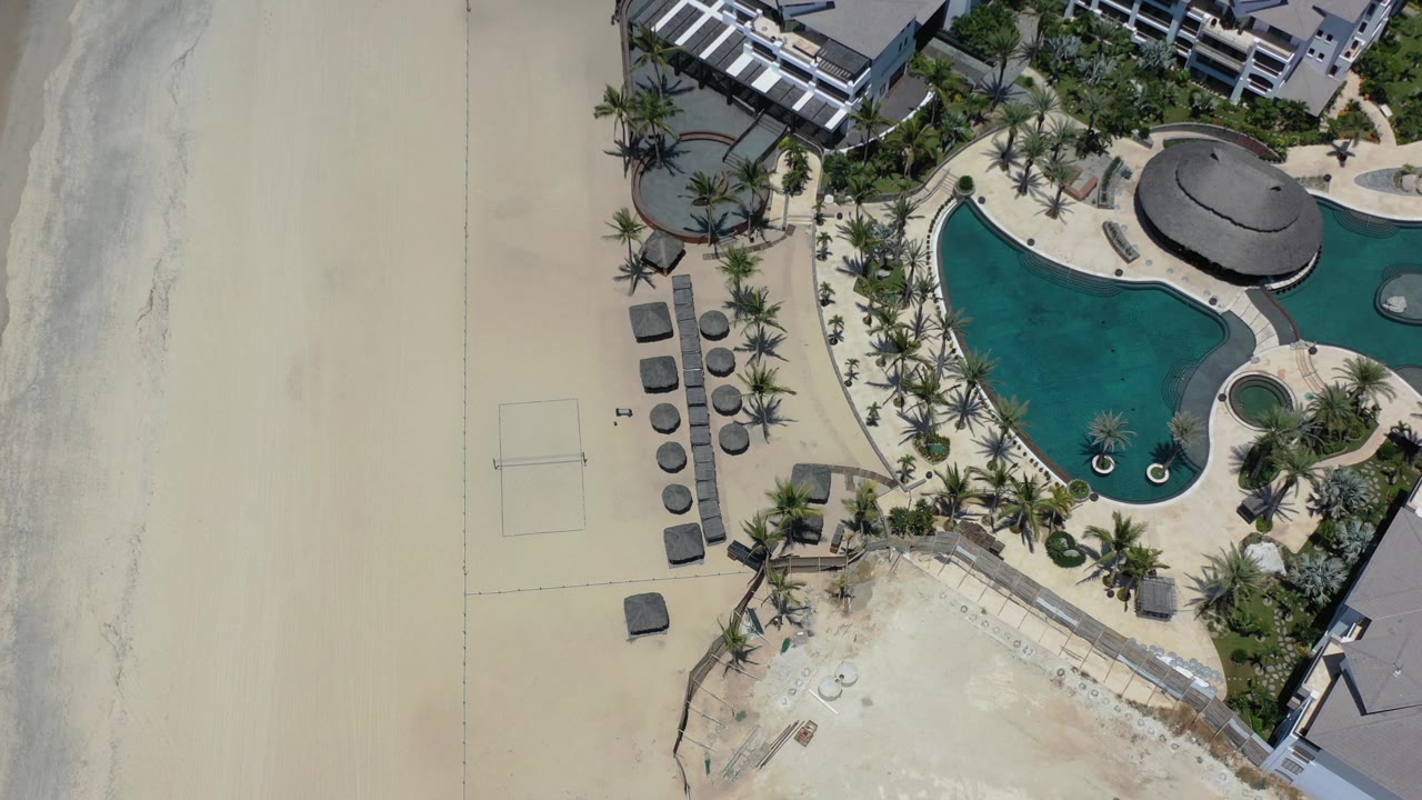 Top-down resort pool area beside a wide beach.
