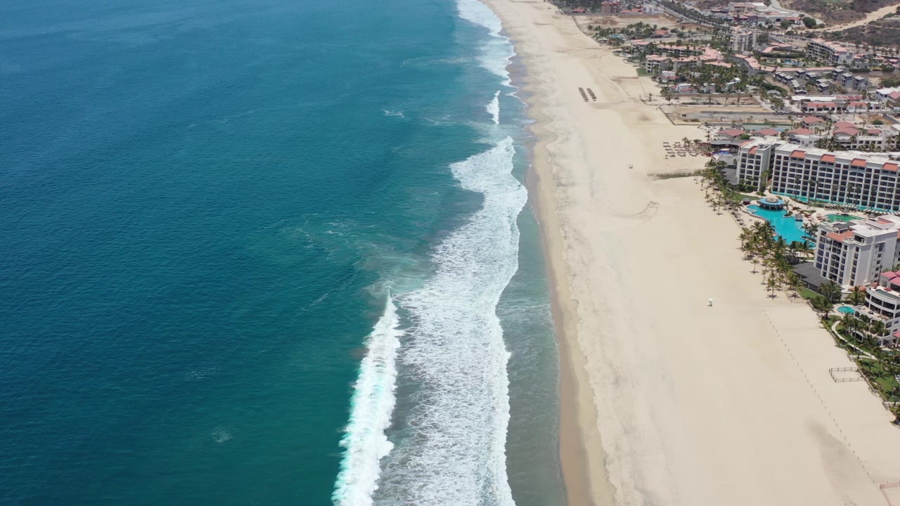 Aerial view of ocean surf, sandy beach, and resort buildings.