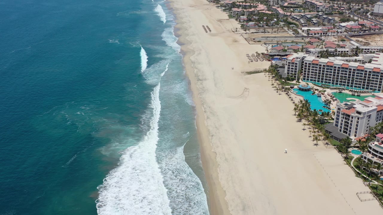 High aerial coastline with surf, beach, and resort buildings.