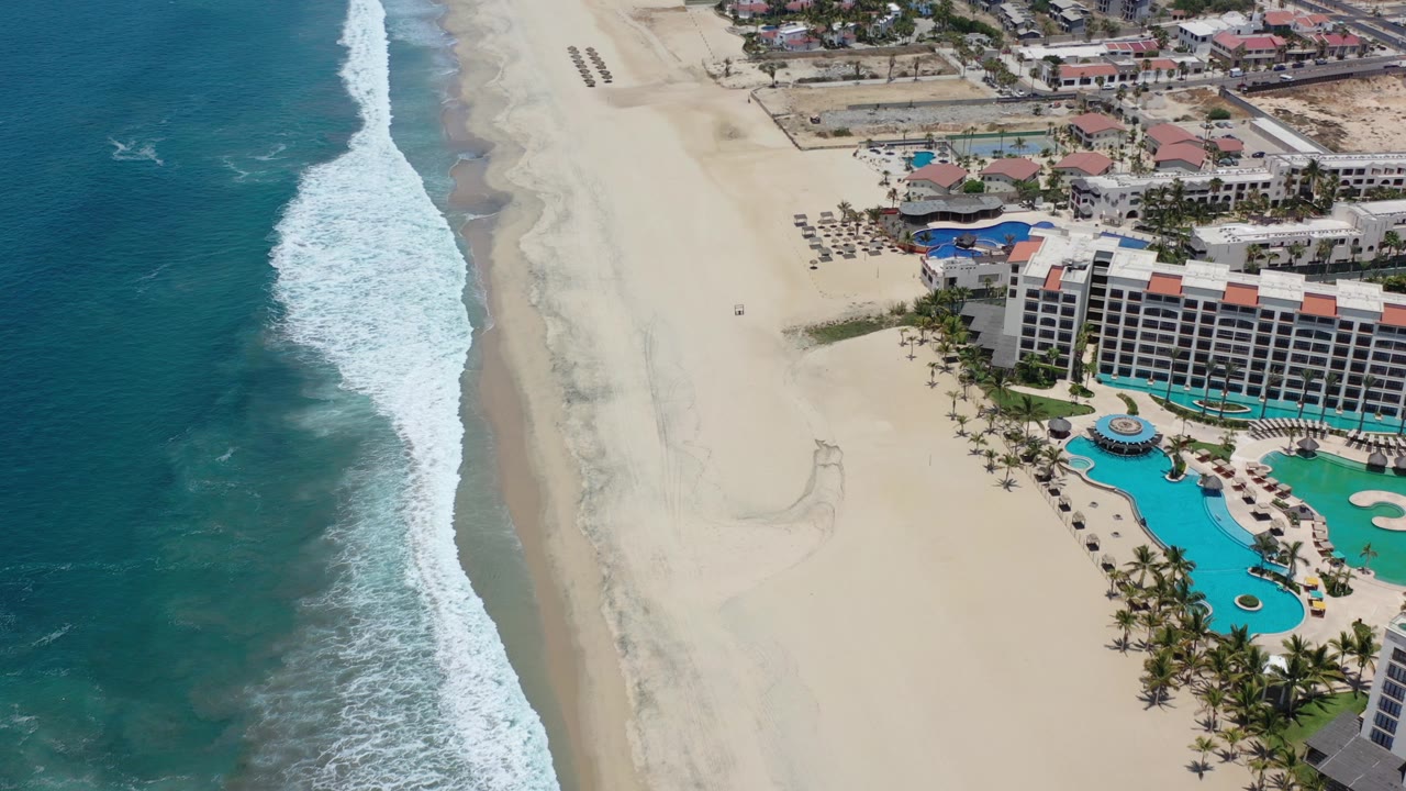 Overhead view of surf, sand, and a beachfront resort with pools.