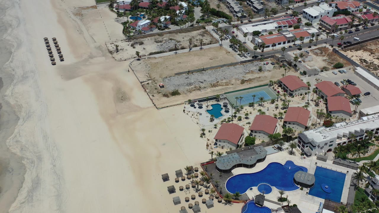 Aerial view of beachside resort buildings, pools, tennis court, and empty sand.