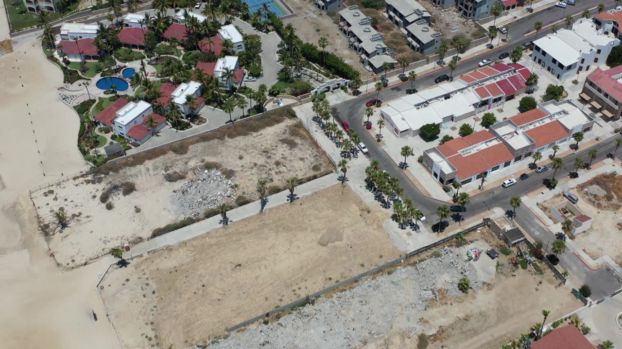 Aerial view of beachside buildings, sandy lots, streets, palms, and pools.