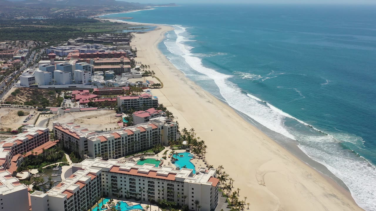 Drone-like view of resort pools and waves along a broad beach