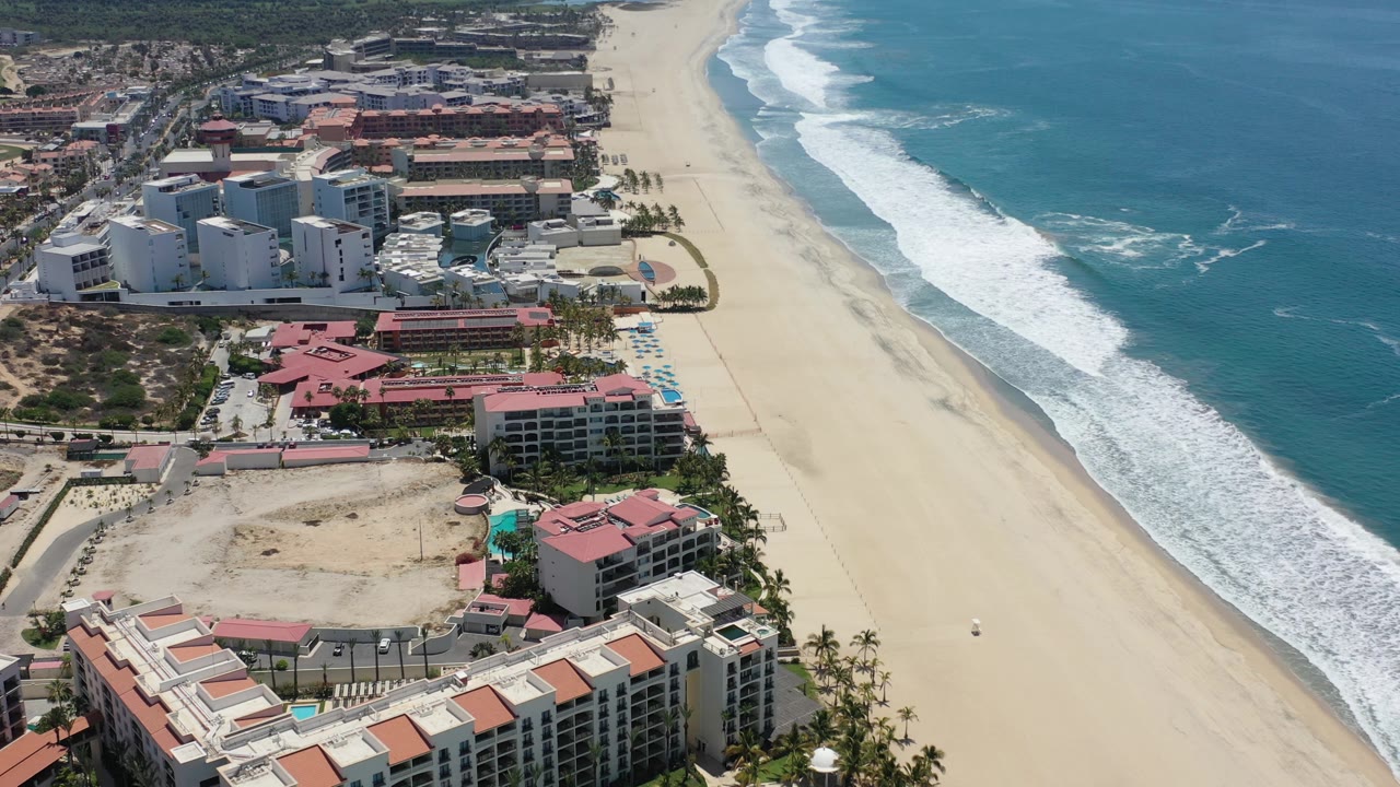 Overhead coastline view with hotels on the left and waves along the beach.
