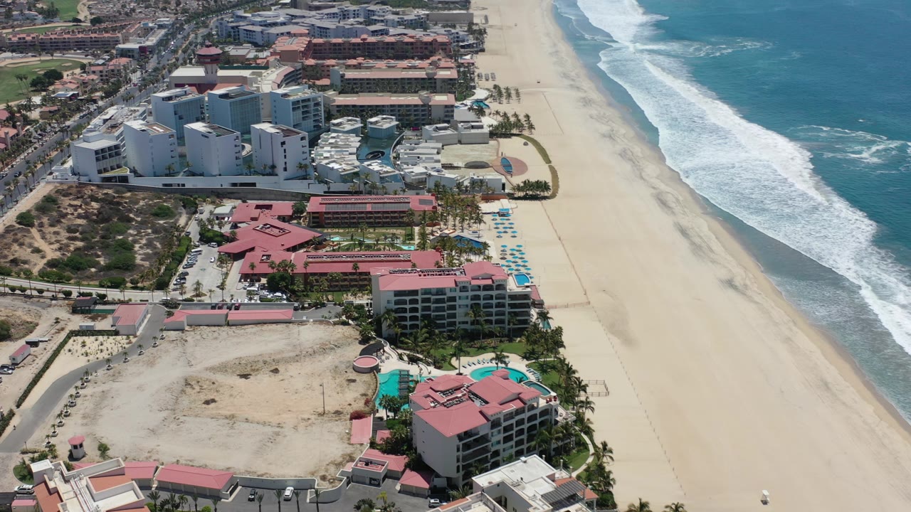 Oblique aerial view of Los Cabos resorts, shoreline, and ocean waves.
