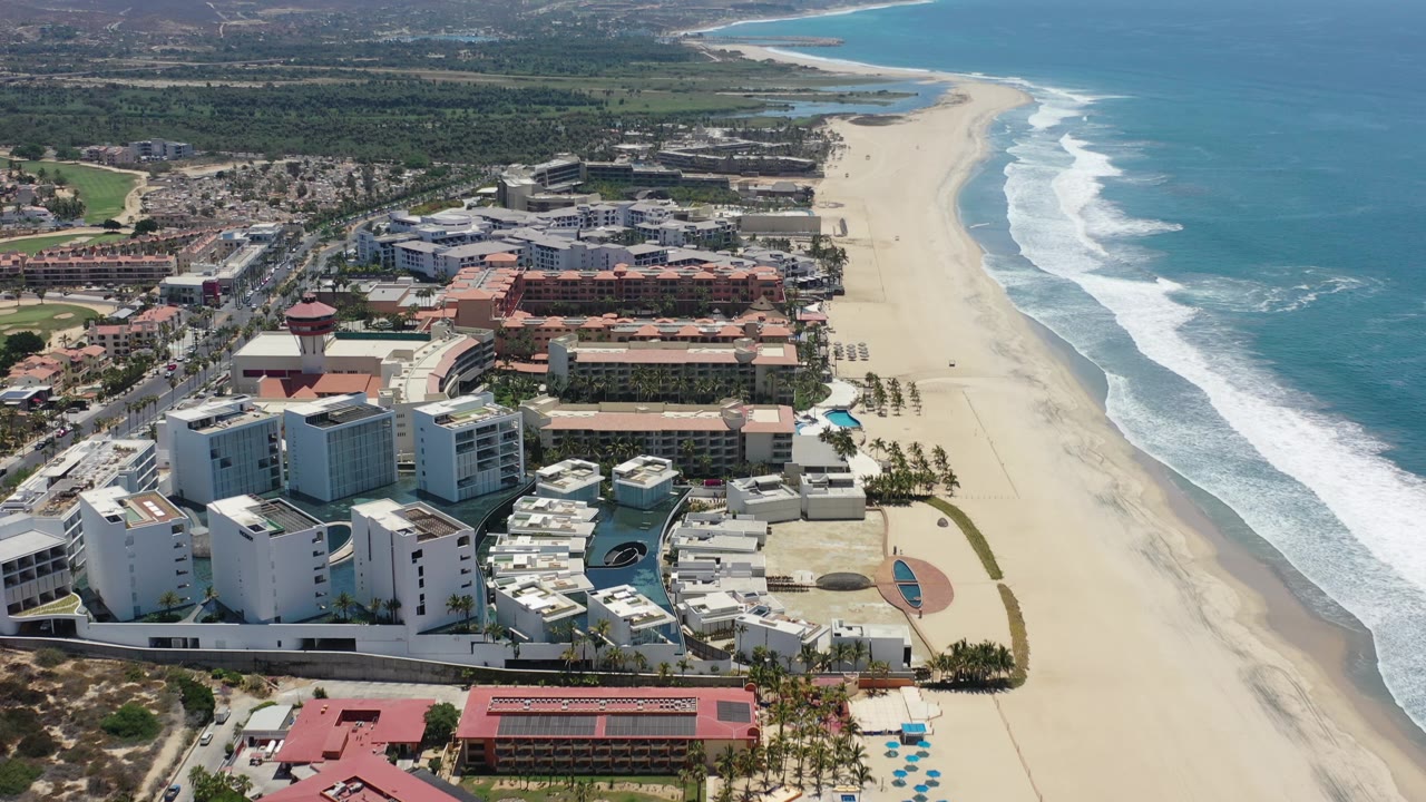 Elevated view of resort rooftops, beach sand, and blue ocean on the right.