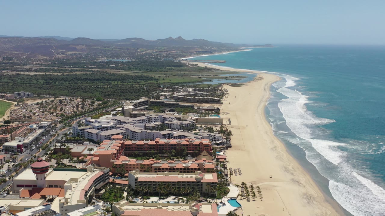 Aerial view of resort buildings beside a wide sandy beach and blue ocean.