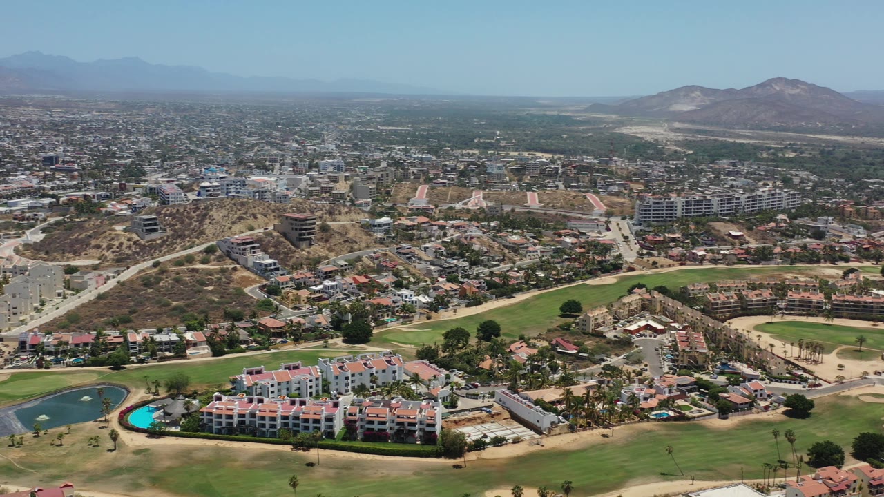 Aerial view of golf fairways, resort buildings, city blocks, and distant mountains.